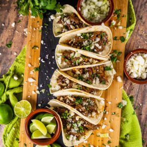 row of barbacoa beef tacos with lime and queso fresco on a tray