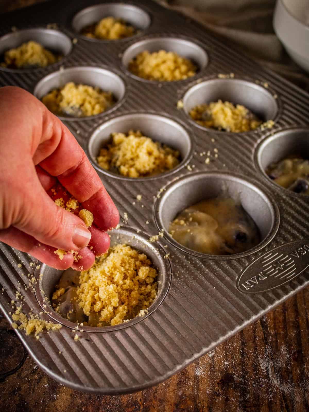 hand sprinkling streusel topping on muffin batter