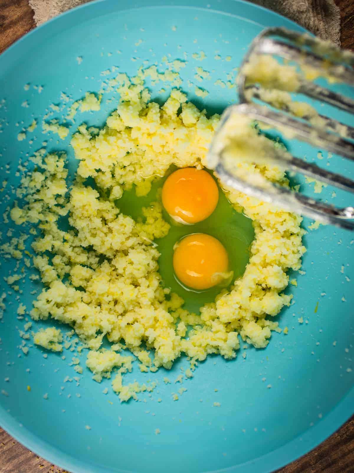 eggs in a blue mixing bowl with creamed butter and sugar