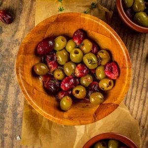 wooden bowl with roasted green olives and purple grapes