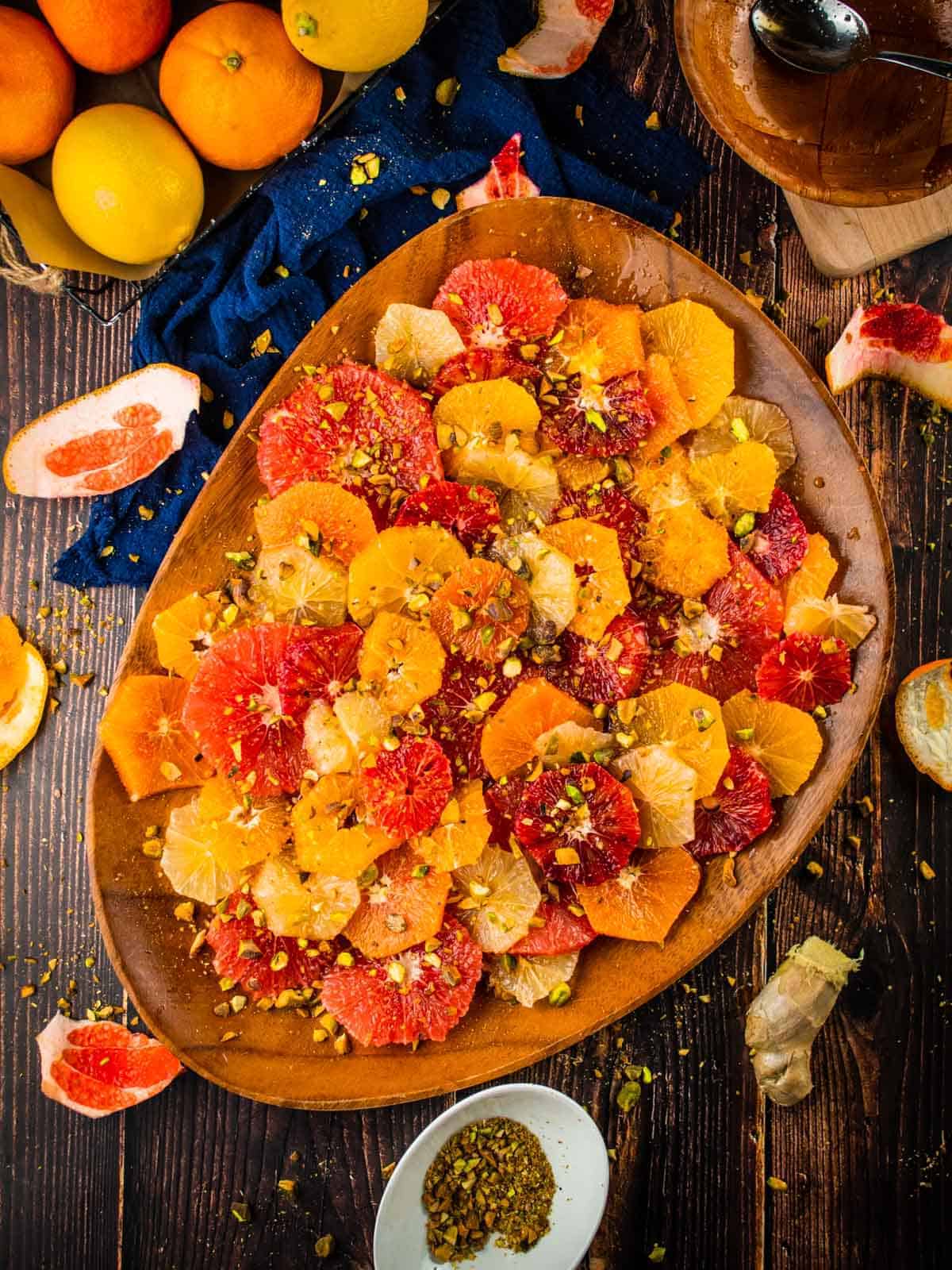 sliced citrus salad on a brown tray topped with chopped pistachios with citrus and peels around 