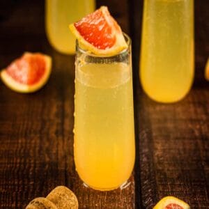 champagne flute with grapefruit cocktail topped with wedge of grapefruit