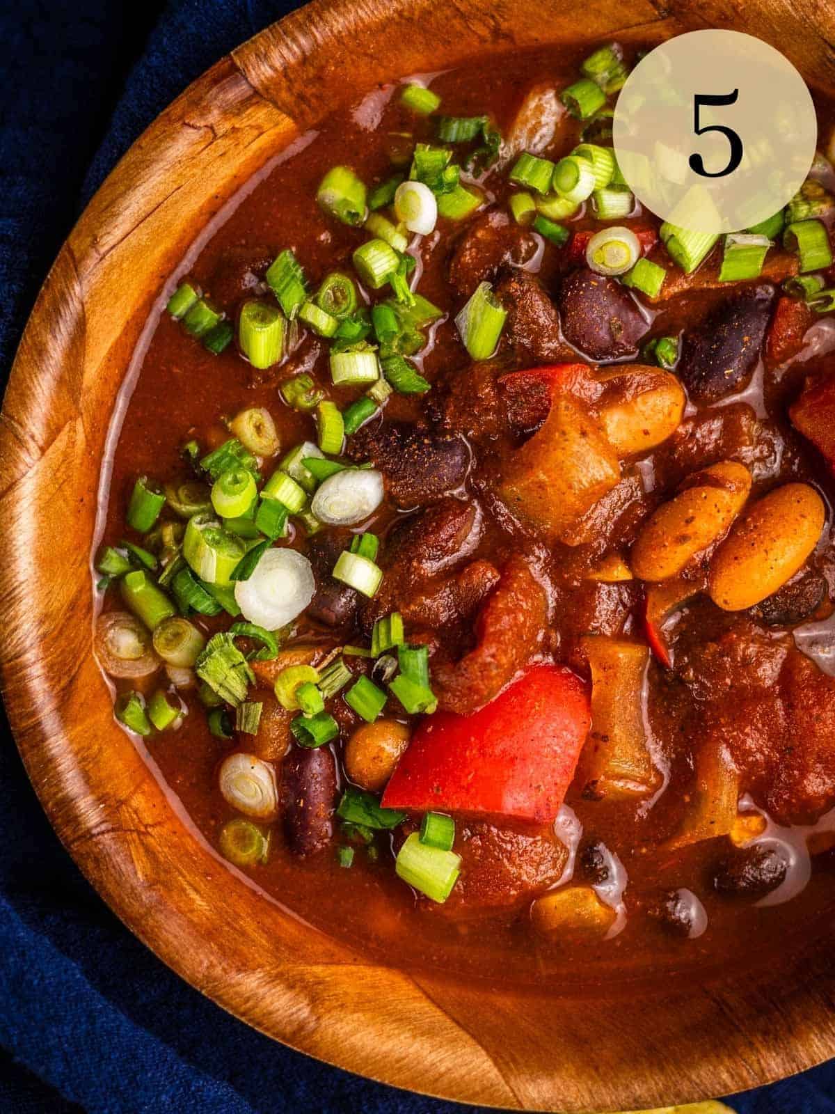 wooden bowl filled with vegan chili with beans garnished with sliced green onions on top