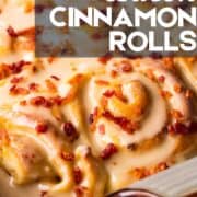 baked cinnamon rolls in a pan with maple icing and crispy bacon on top.