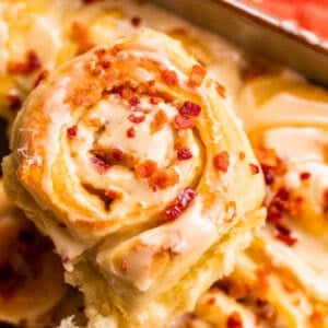 close up of a cinnamon roll with icing and crispy bacon on it.