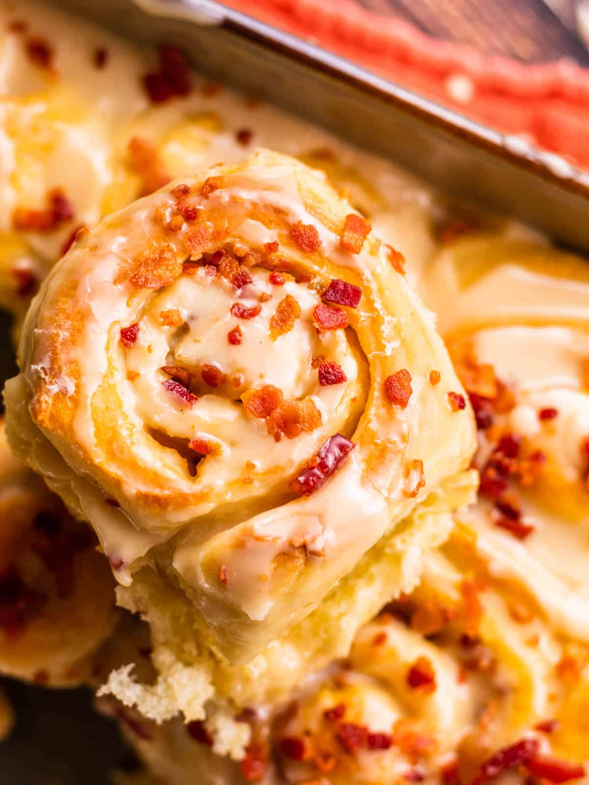 close up of a cinnamon roll covered in icing and crispy bacon pieces.