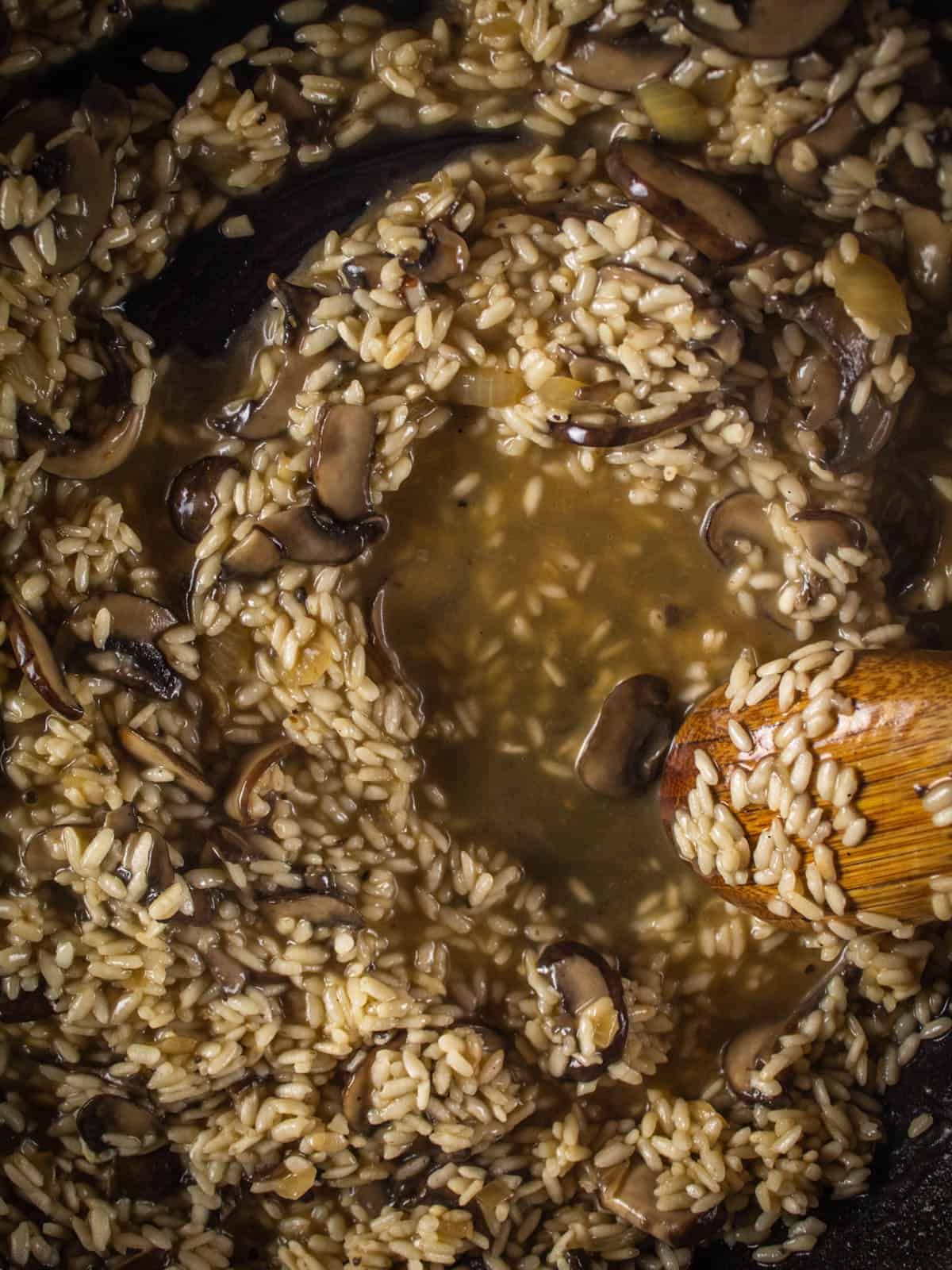 arborio rice with mushrooms and vegetable broth in a skillet