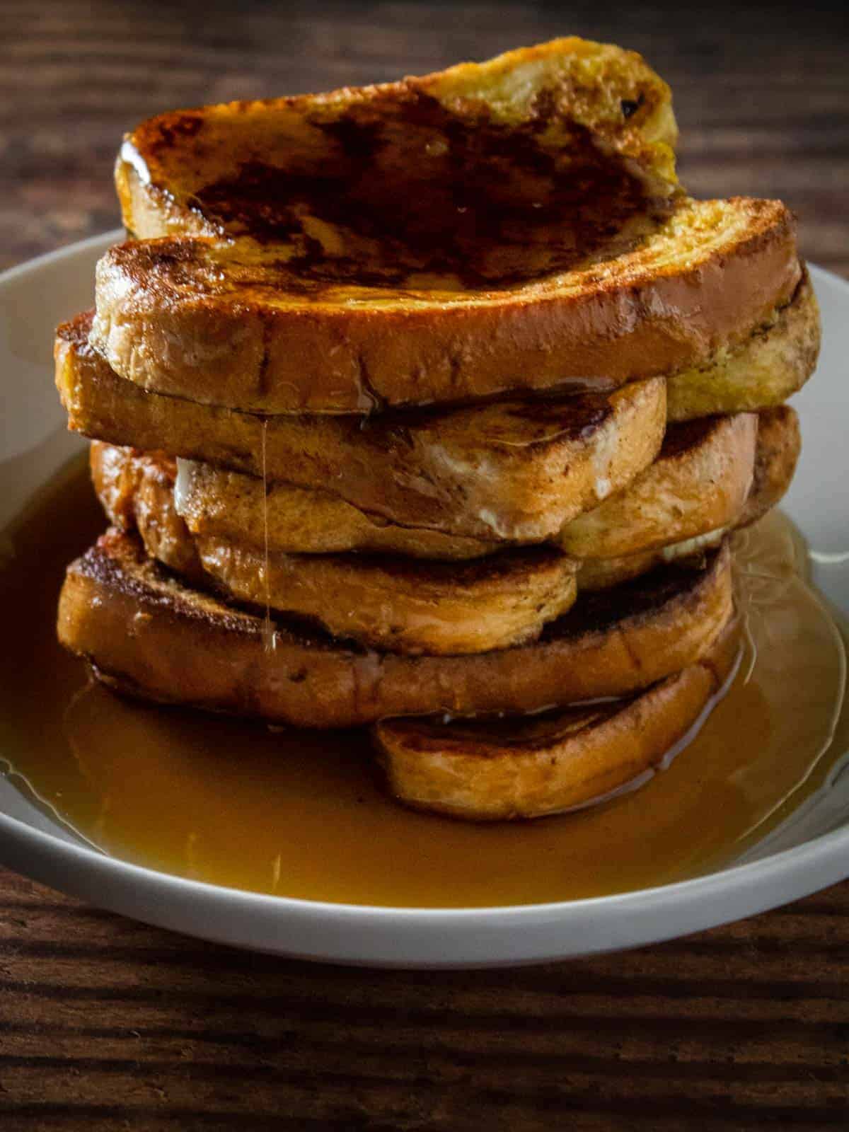 stack of seven slices of french toast on a white plate covered in maple syrup 
