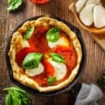 pizza in a cast iron skillet with tomatoes, cheese and fresh basil