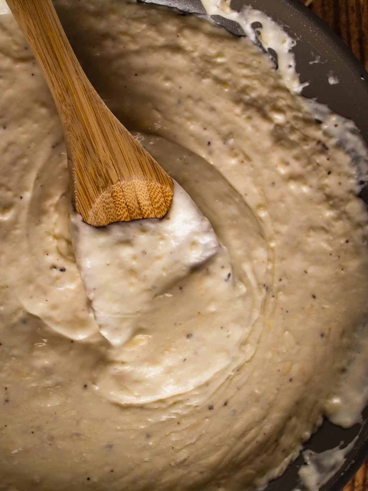 thick and creamy homemade alfredo sauce being stirred with wooden spoon in a skillet