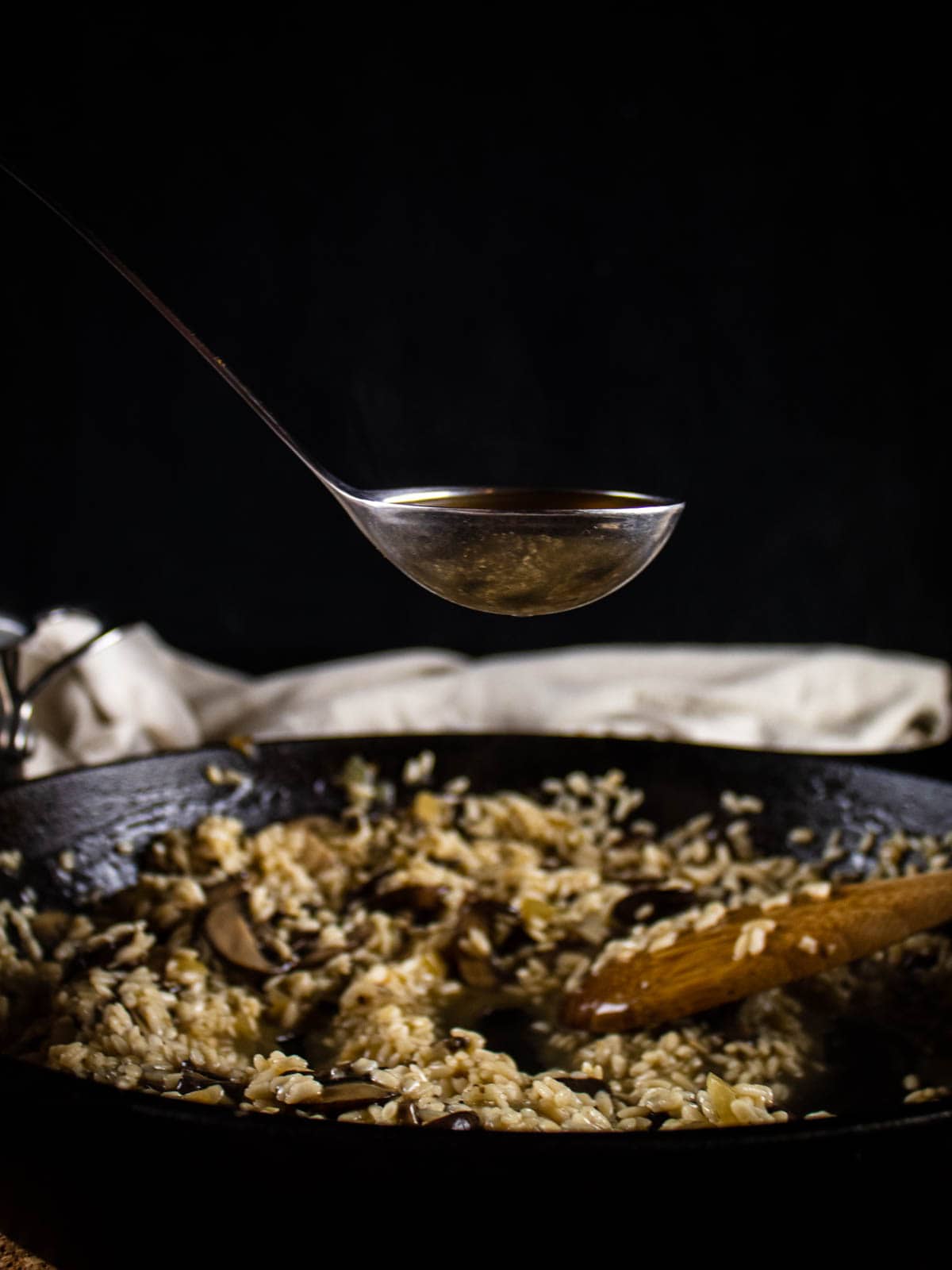 ladle of broth over a skillet of risotto