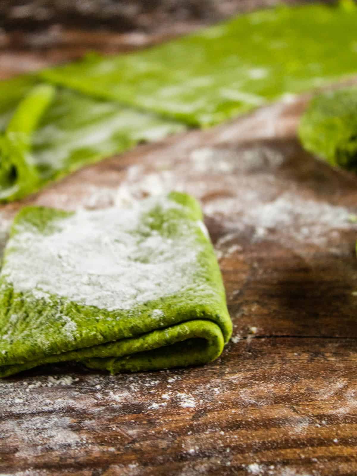 folded sheets of spinach pasta dough with flour