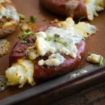 smashed red potatoes on a sheet pan topped with melted blue cheese