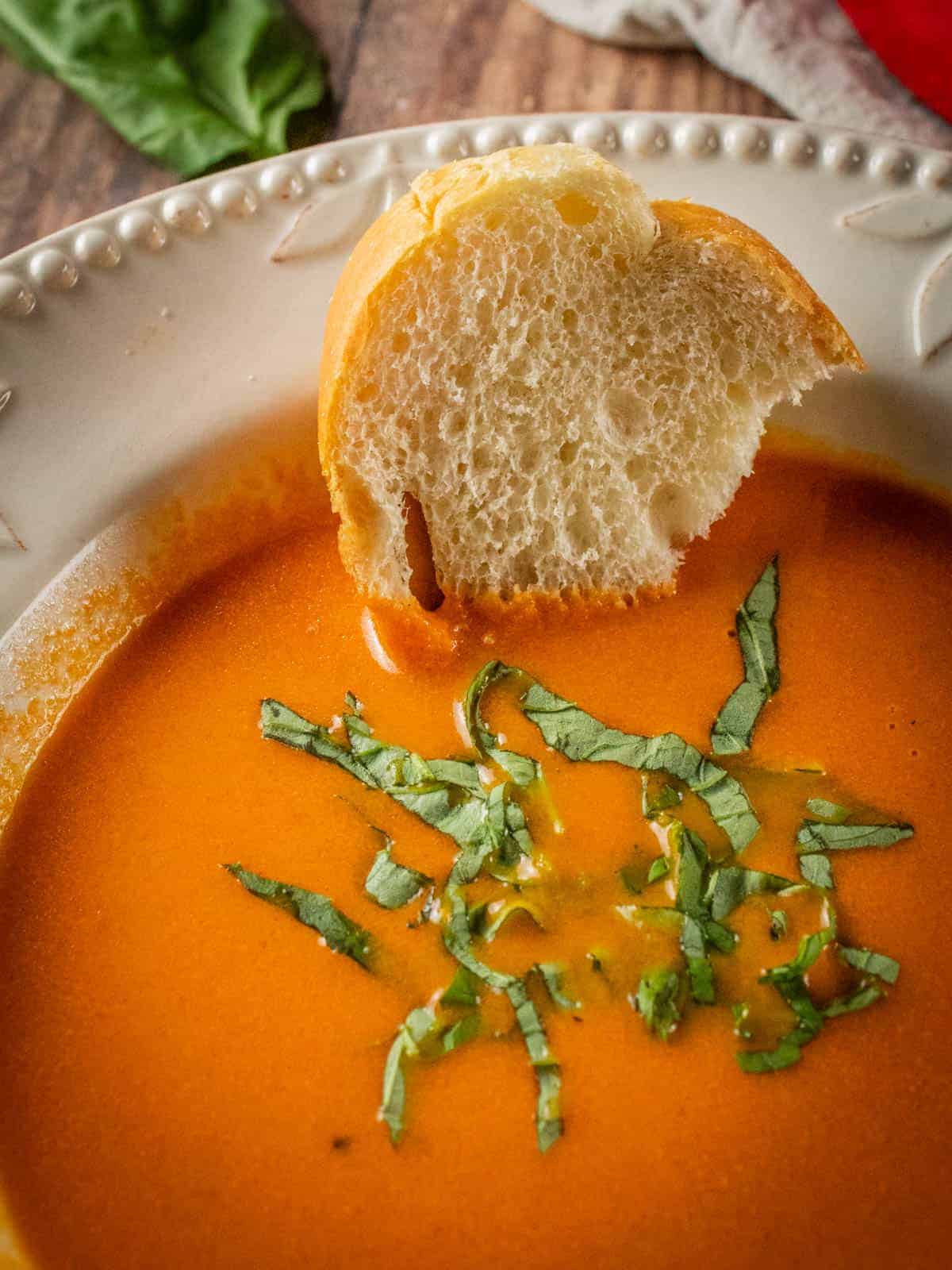 bowl of tomato mascarpone soup topped with fresh basil and piece of bread into it.