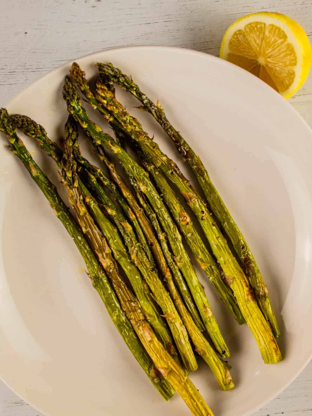 roasted asparagus stalks on a white plate with a lemon half next to it