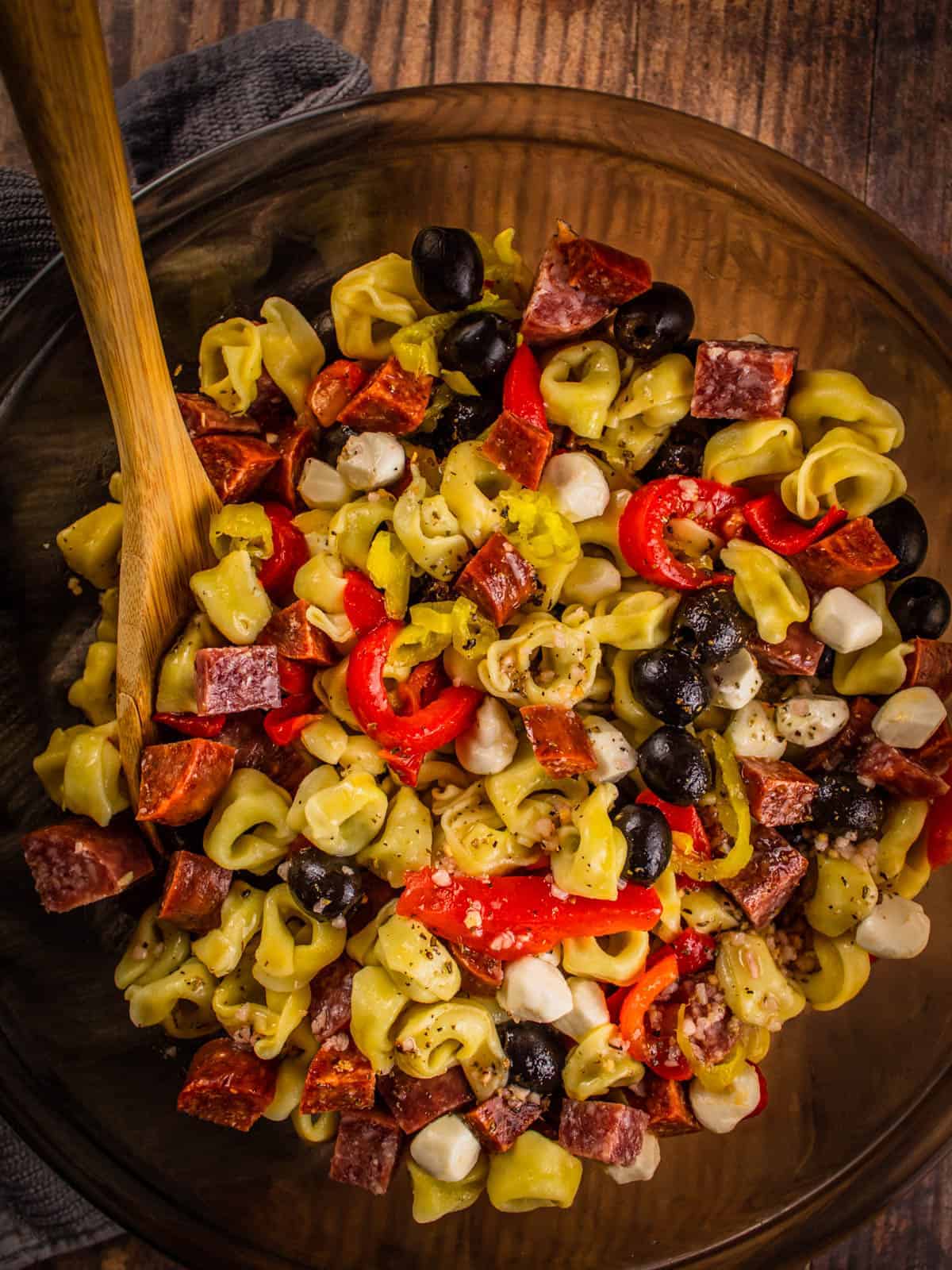 antipasto salad with tortellini, meat, cheese and peppers in a bowl with wooden spoon.