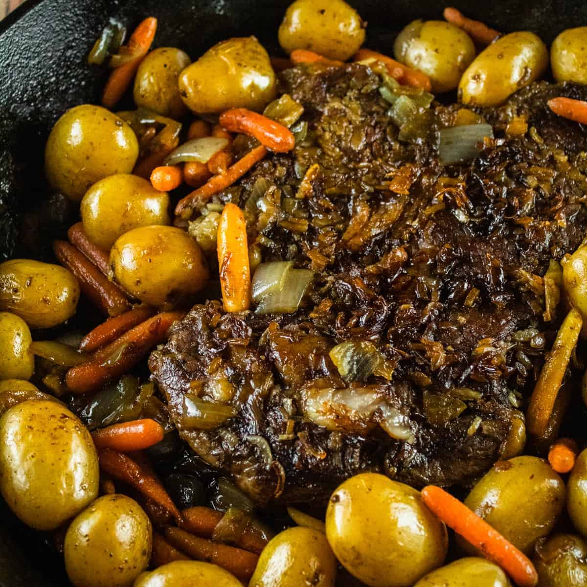 cooked beef roast with potatoes and carrots in a cast iron skillet