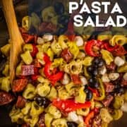 wooden spoon stirring antipasto pasta salad in a bowl.