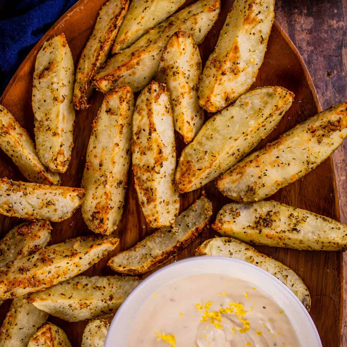 crispy potato wedges on a wooden tray with lemon aioli dip in a white bowl