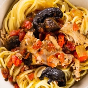 chicken cacciatore with mushrooms and tomatoes on spaghetti noodles in a bowl.