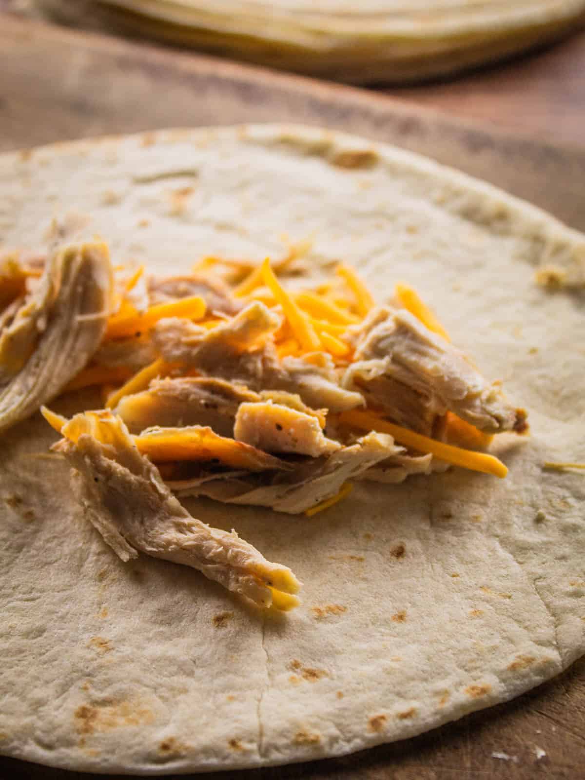 shredded cheese and chicken on a flour tortilla
