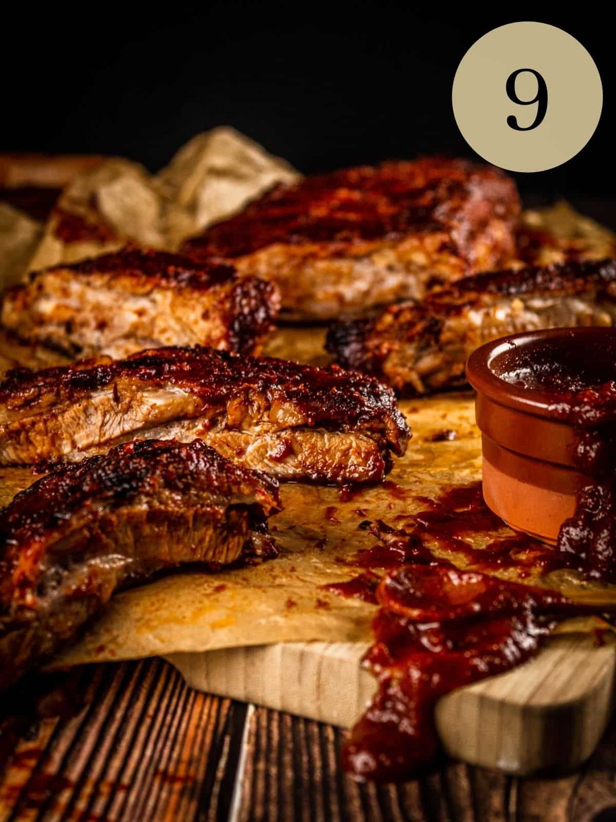 ribs cut into slices on a cutting board with barbecue sauce on dripping on them.