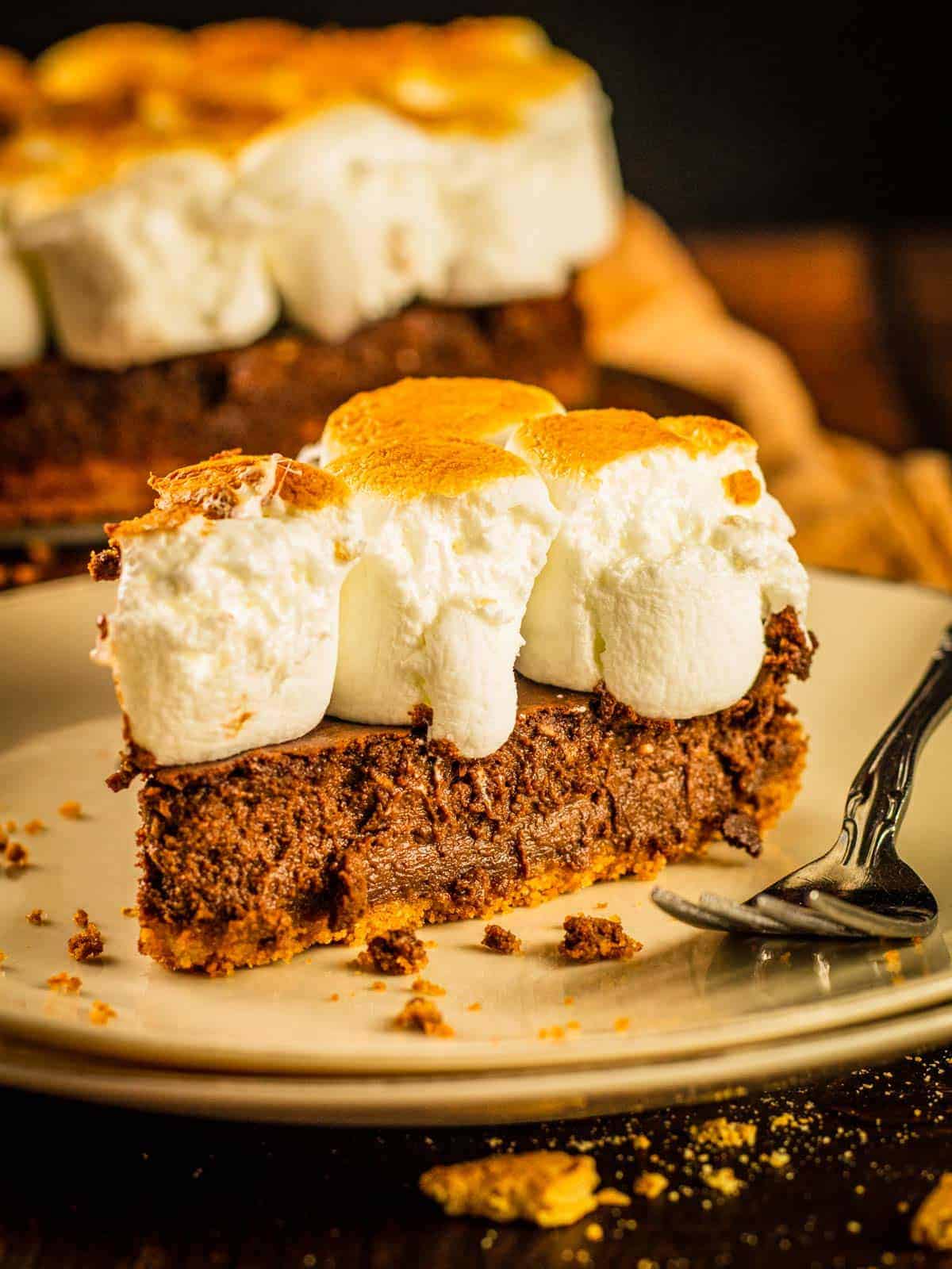 slice of chocolate cheesecake topped with toasted marshmallows on a plate with fork next to it.