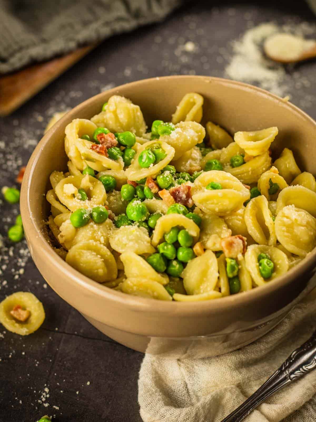 tan bowl filled with orecchiette pasta, pancetta, peas and parmesan cheese