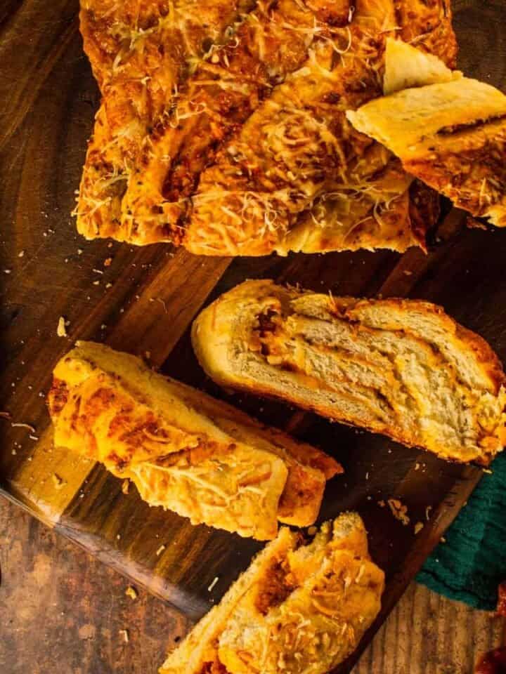 sliced braided bread with cheese and marinara on a wooden cutting board with a knife