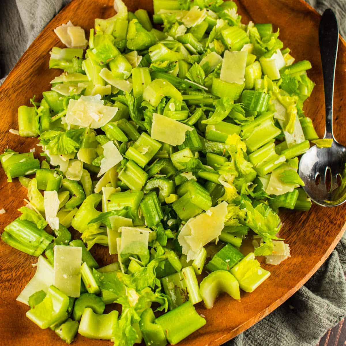 chopped celery salad with parmesan shavings on a wooden platter with a metal spoon