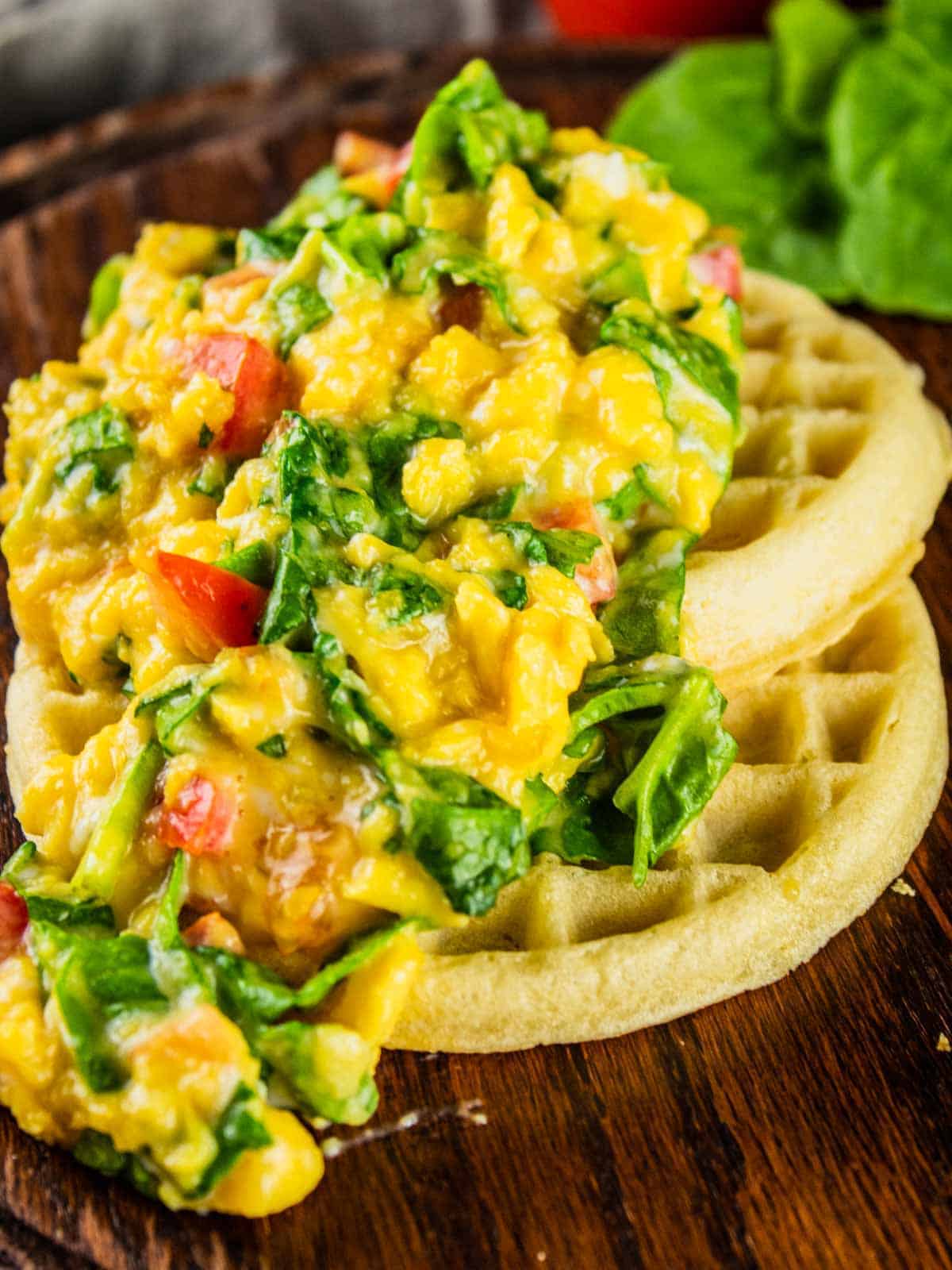 soft scrambled eggs mixed with spinach and tomato on top of waffles