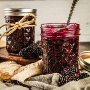 two mason jars filled with homemade blackberry jam with fresh blackberries around it