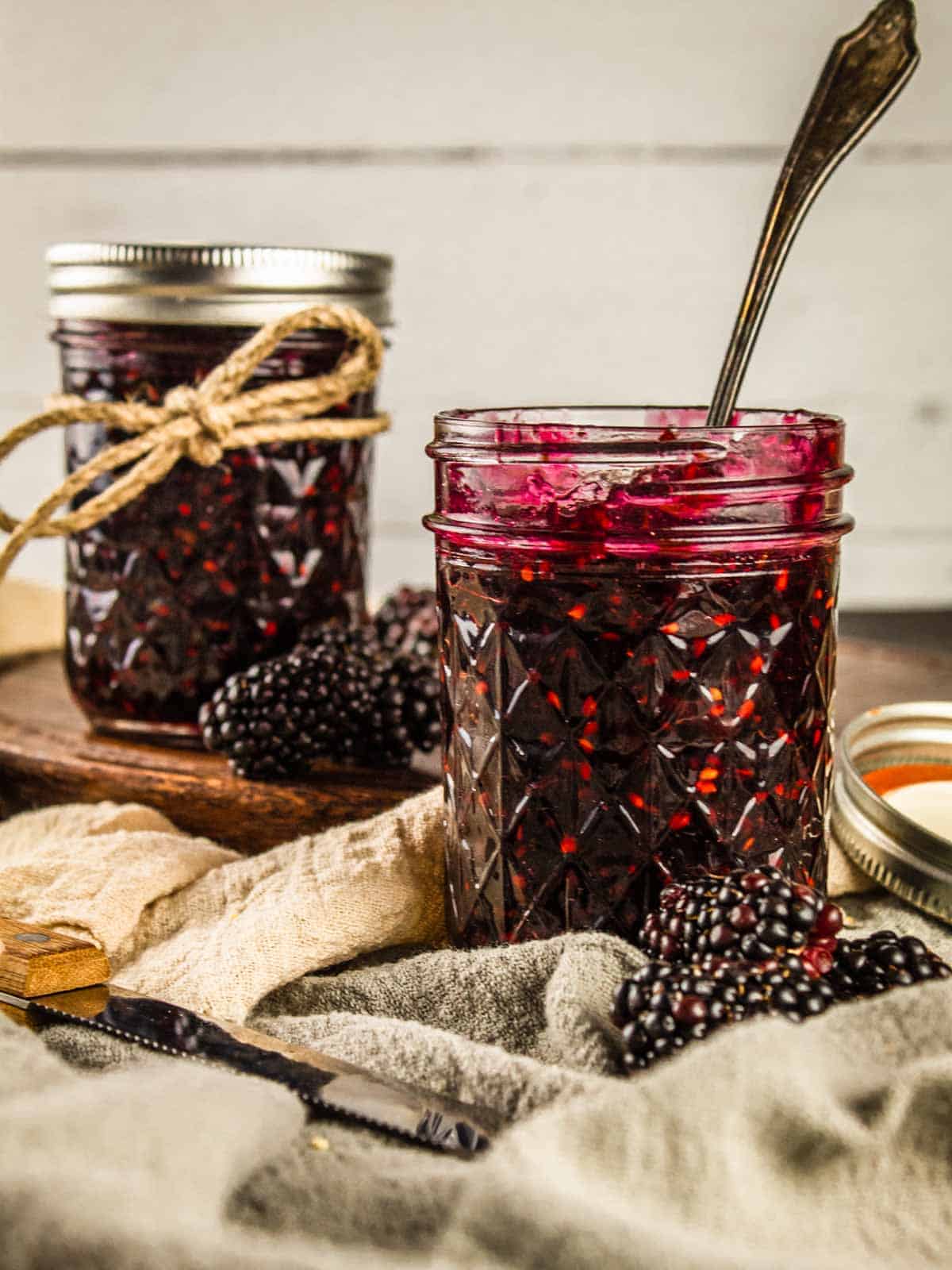 two mason jars with blackberry jam and fresh blackberries around them