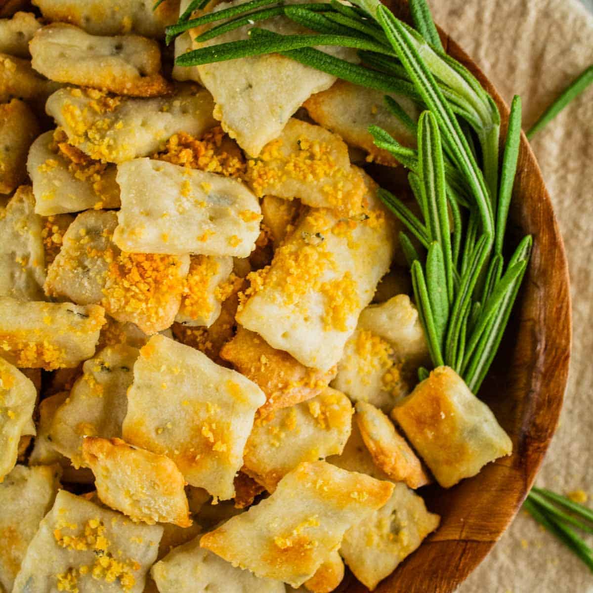 wooden bowl filled with homemade rosemary and parmesan square crackers with a sprig of rosemary
