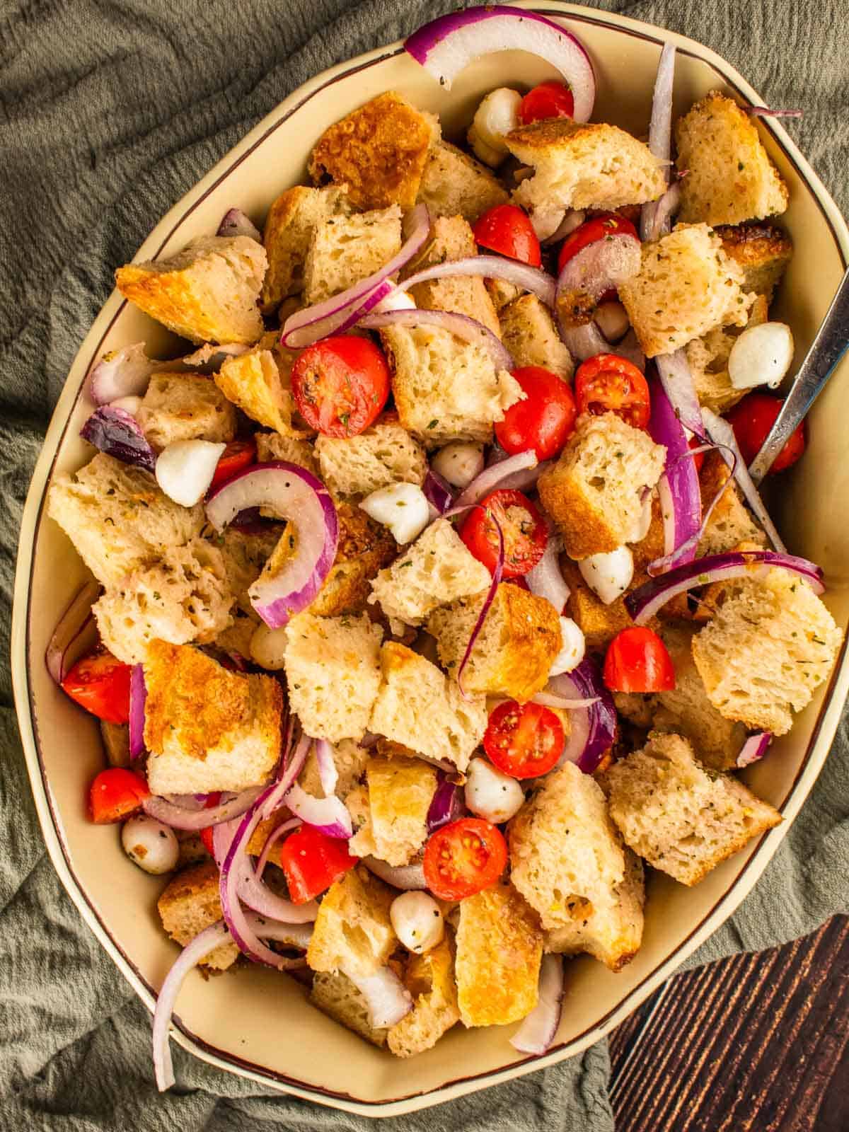 summer panzanella salad with tomatoes, cheese and onions in a ceramic dish