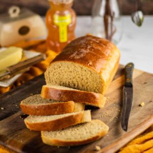 sliced honey wheat bread loaf on a cutting board with a knife and yellow napkin under it