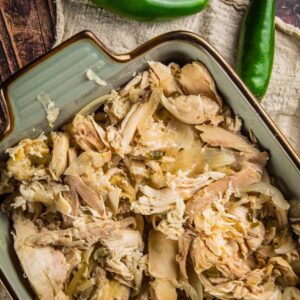 shredded chicken in a blue ceramic dish next to whole jalapenos
