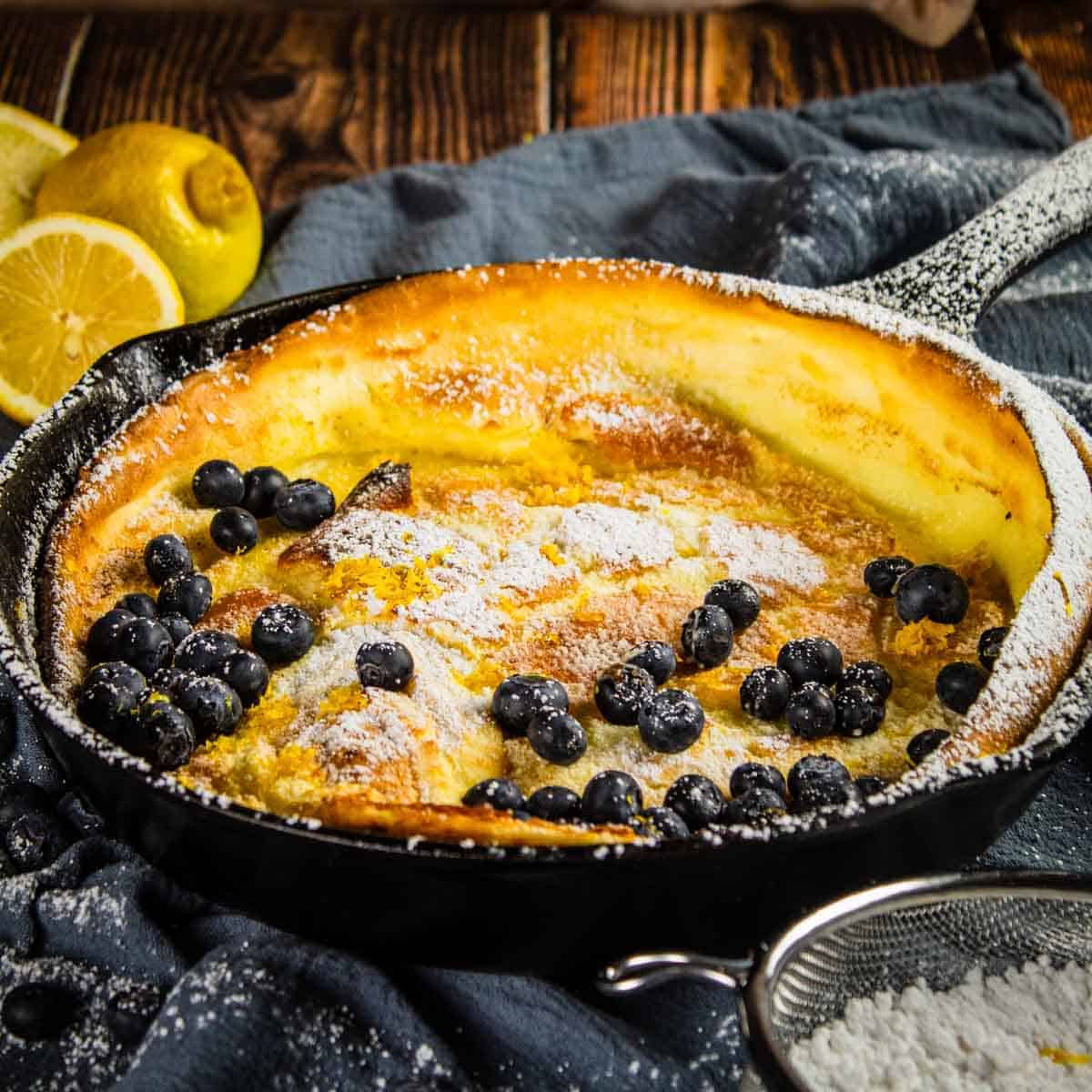 dutch baby german pancake in a cast iron pan topped with fresh blueberries and powdered sugar