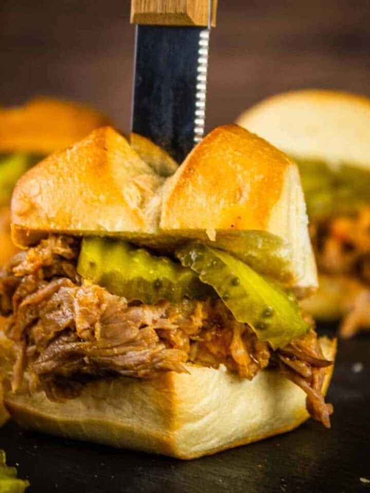 pulled pork slider topped with pickles and a knife sticking in the top of it