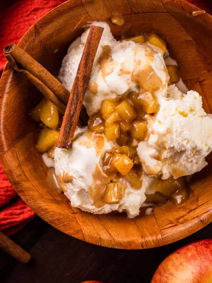 wooden bowl filled with ice cream and apple caramel topping and two cinnamon sticks