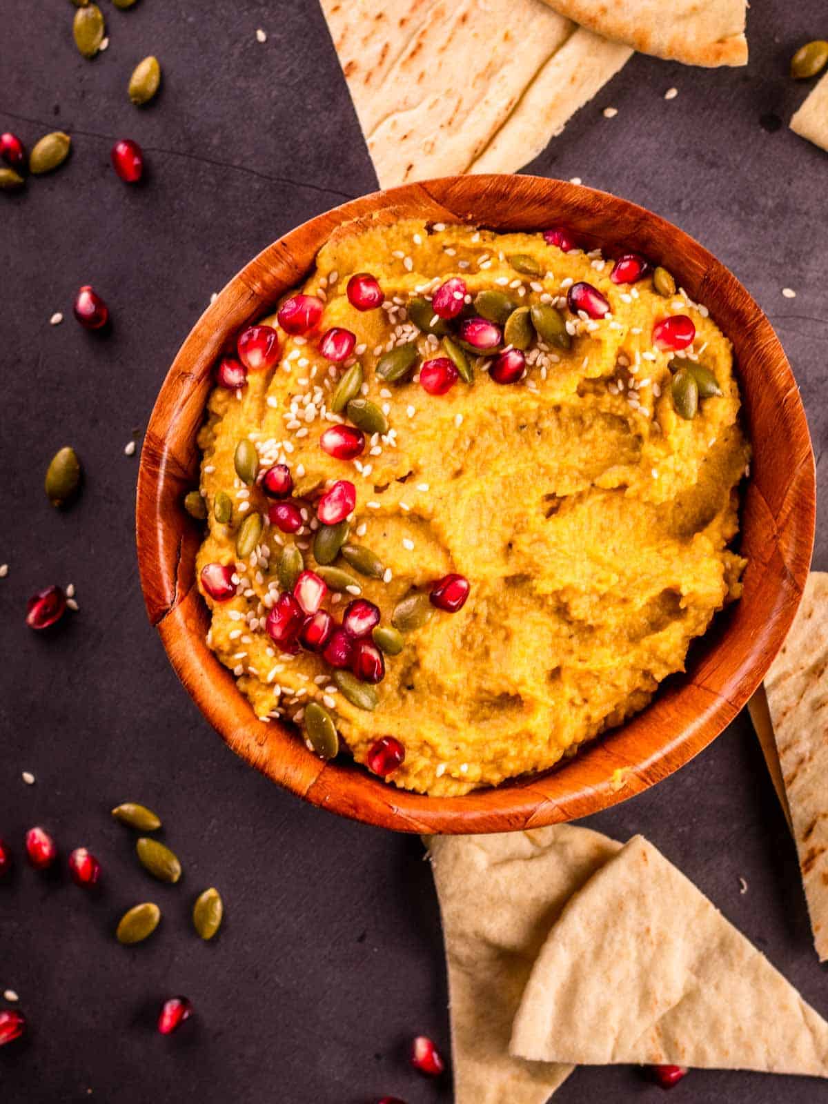 pumpkin hummus topped with pepitas, sesame seeds and pomegranate seeds with pita pieces next to it