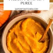 pumpkin puree in a tan bowl with a small wooden spoon next to pumpkins