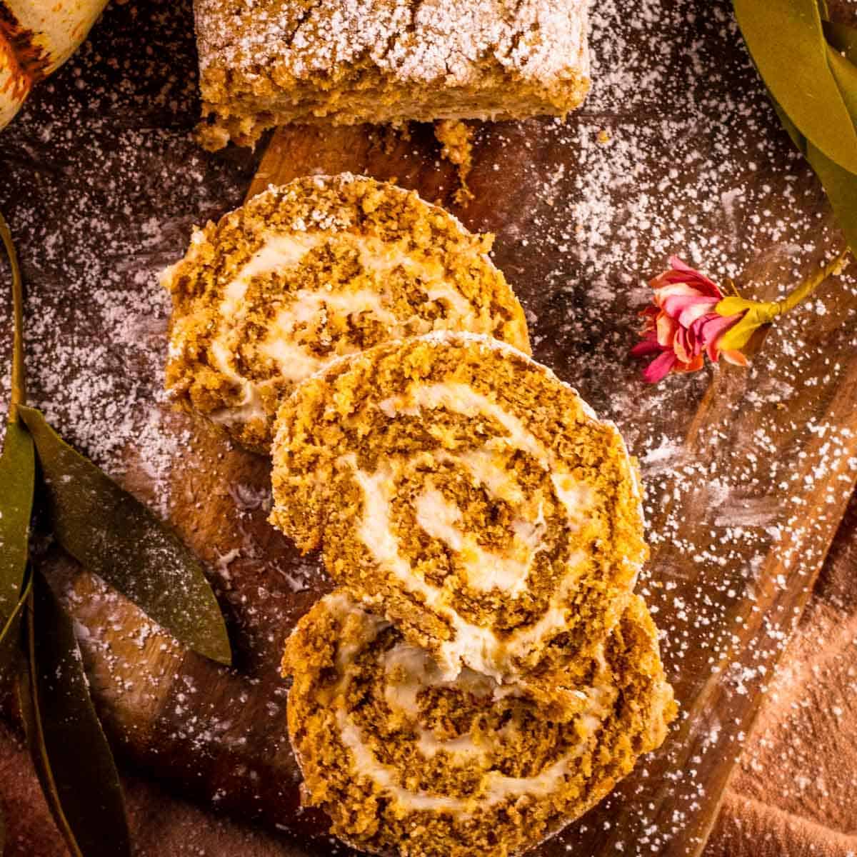 three slices of pumpkin rolls staggered on top of each other on a wooden cutting board 