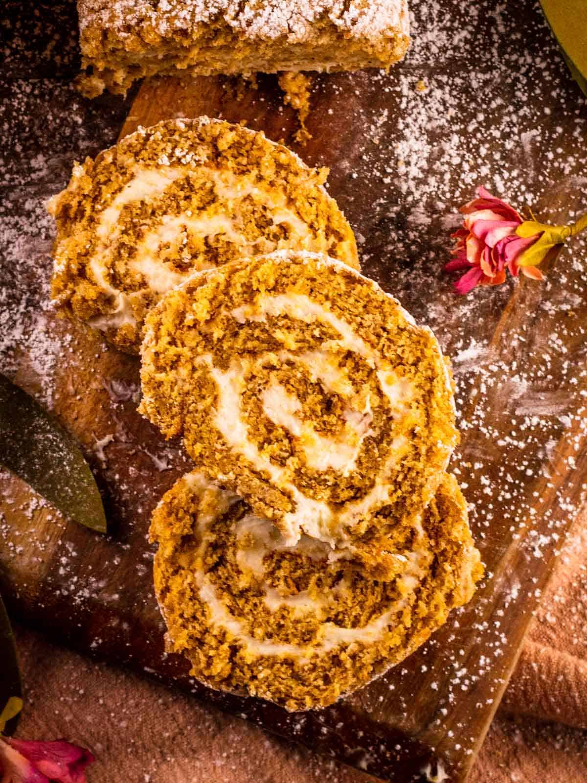 overhead shot of three slices of pumpkin roll stacked on each other next to a flower
