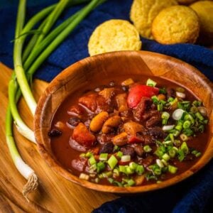 wooden bowl of chili topped with sliced green onions next to green onions and corn muffins