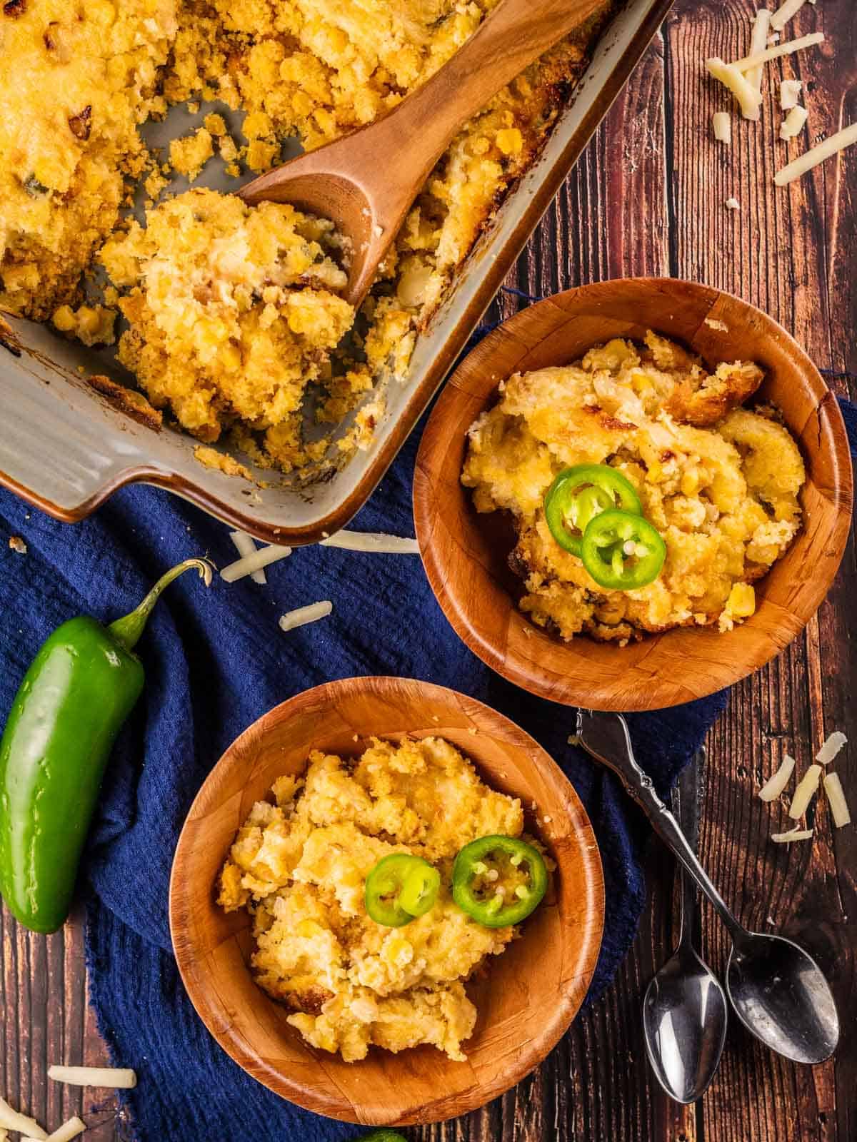 two wooden bowls and pan filled cheddar jalapeno cornbread pudding topped with sliced jalapenos