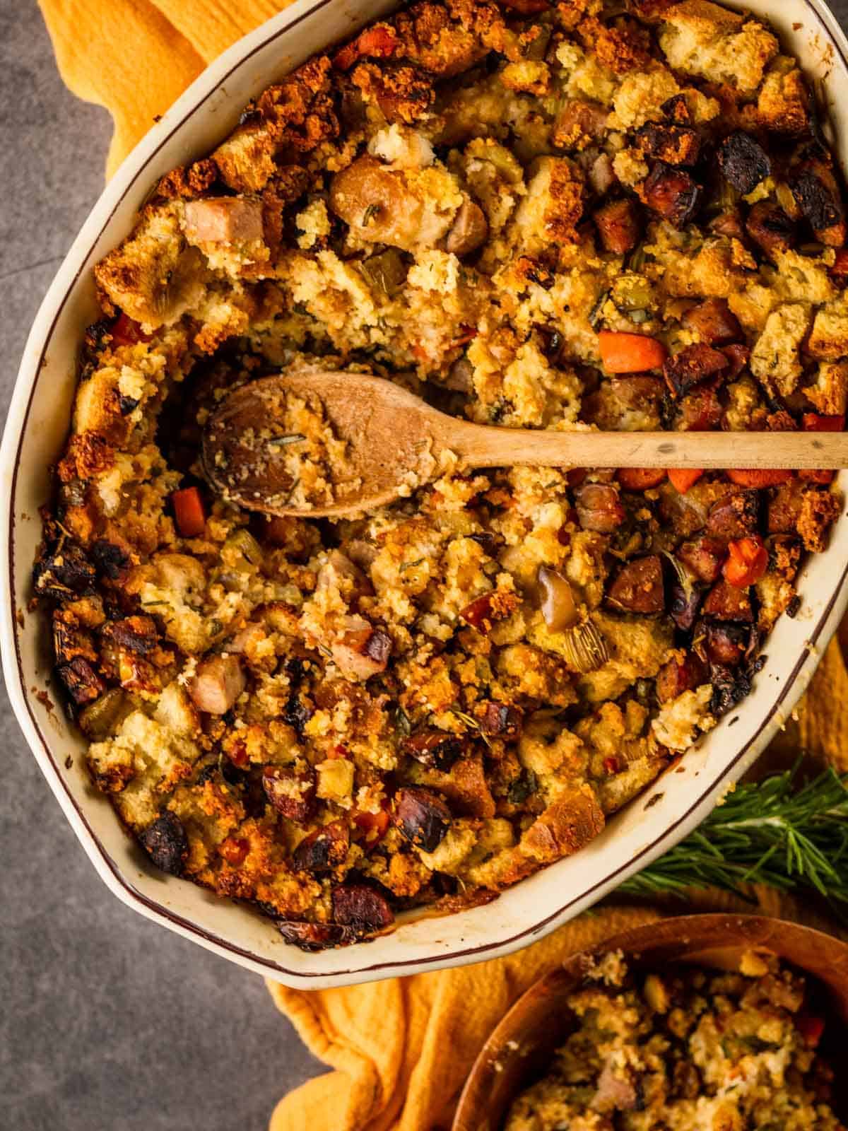 oval baking dish filled with cornbread and sausage stuffing with a wooden spoon scooping it out