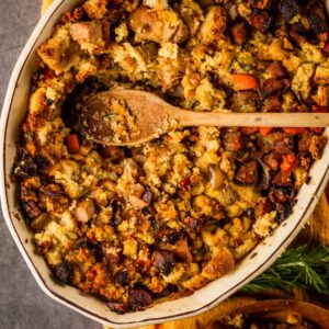 cornbread sausage stuffing in a oval baking dish with a wooden spoon scooping it out