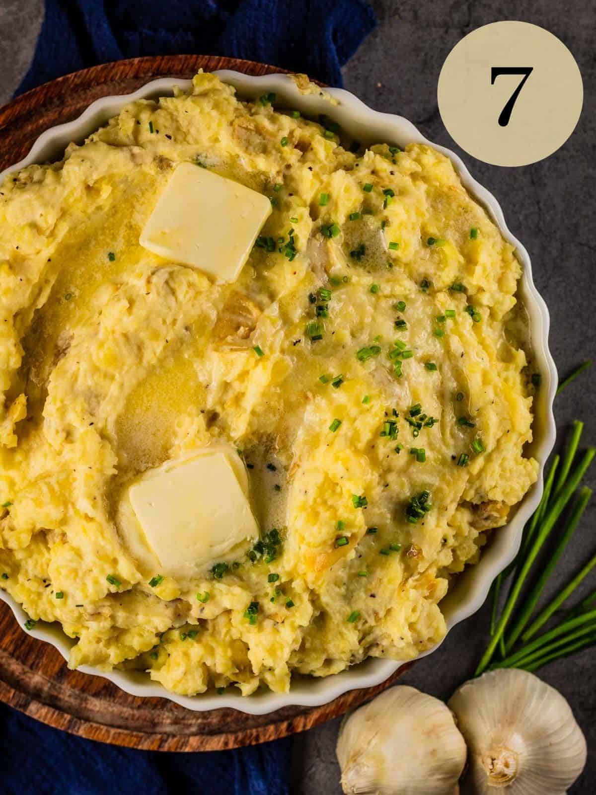 roasted garlic mashed potatoes topped with butter pats and fresh chives in a white dish