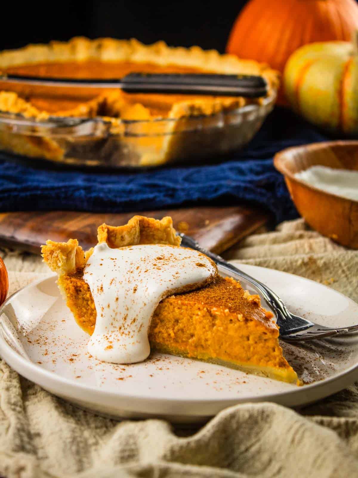 slice of pumpkin pie on a white plate topped with whipped cream and cinnamon